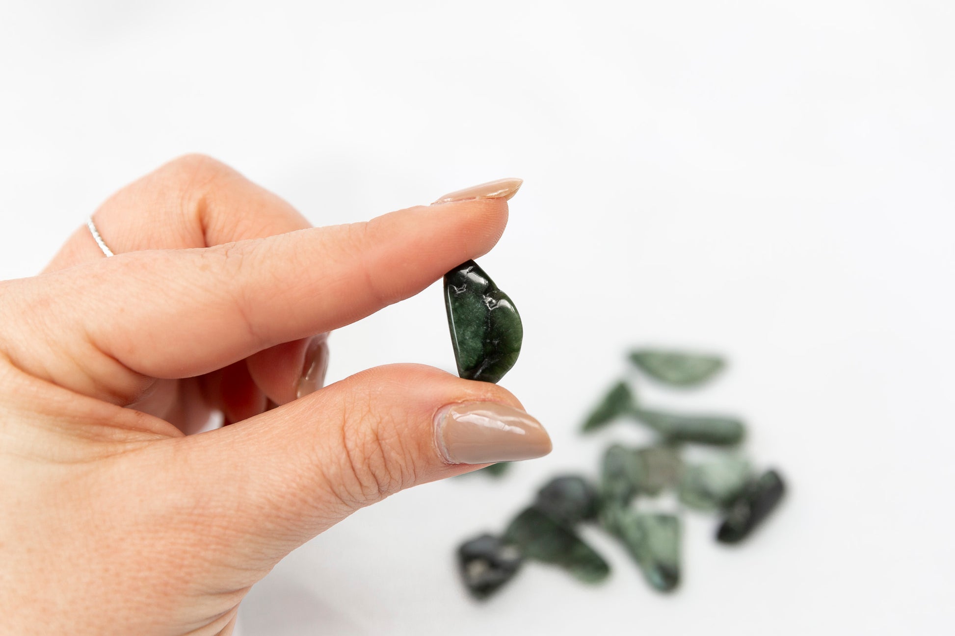 Hand holding a green stone with more stones on a white background