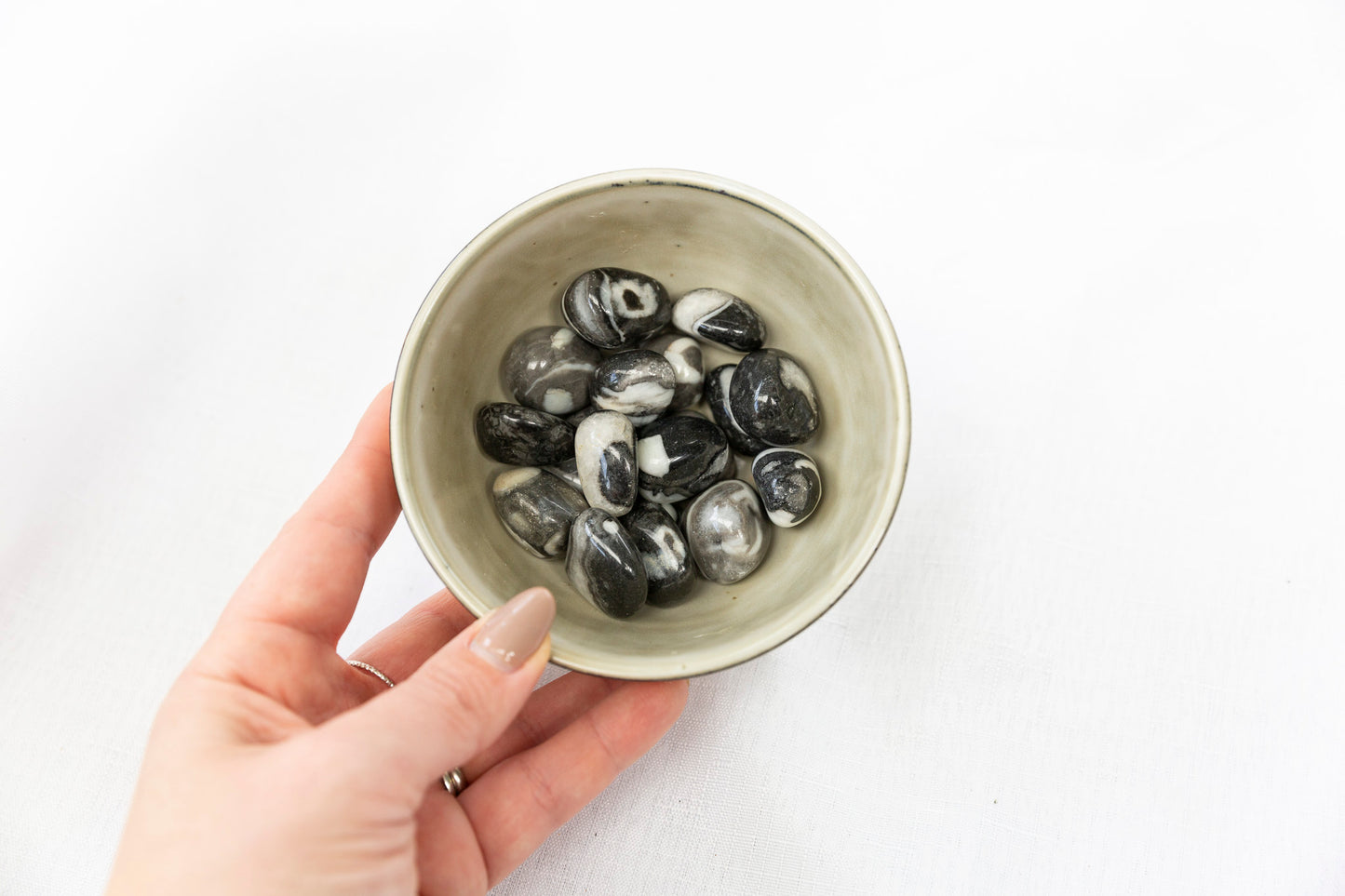 Hand holding a bowl of black and white stones on a white background