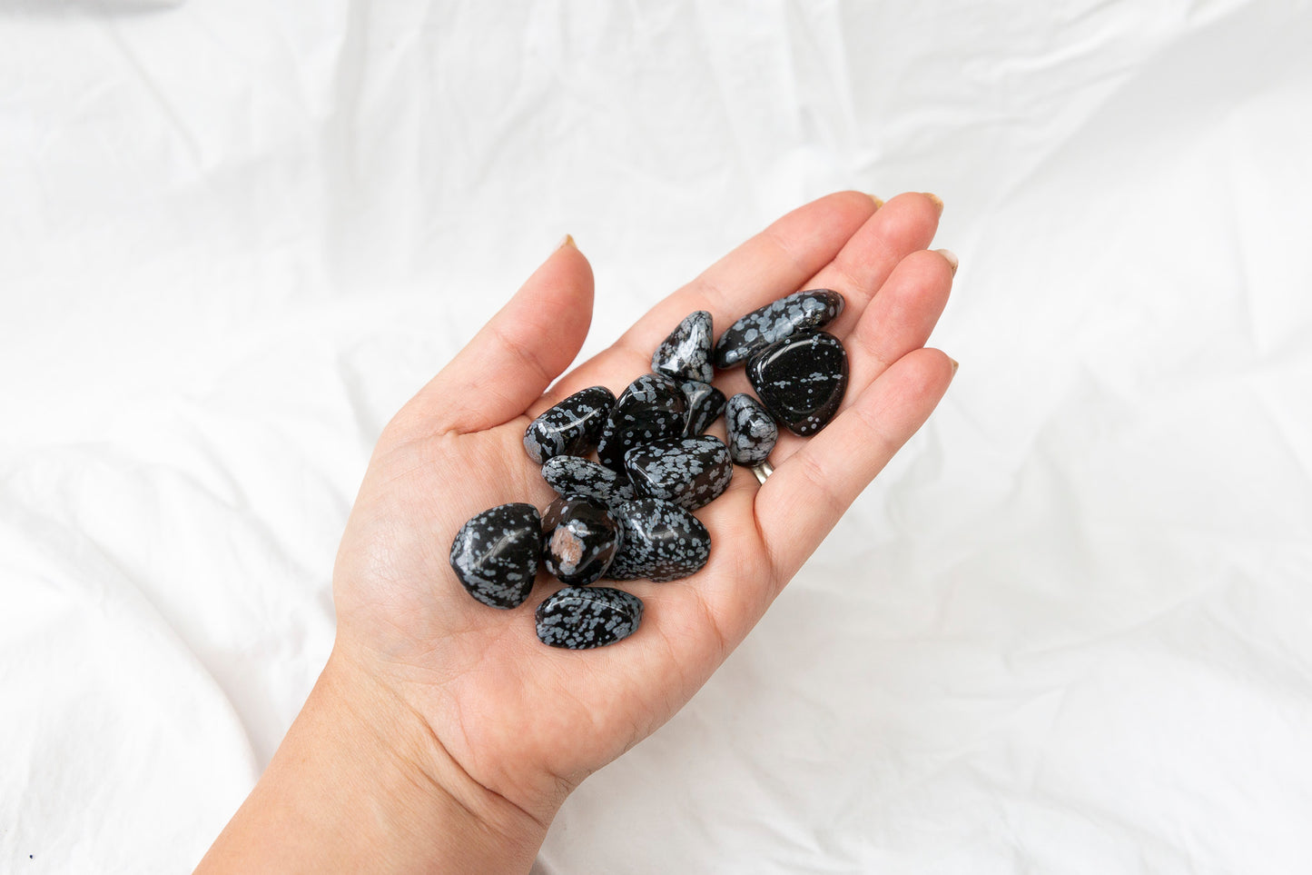 Hand holding black and white snowflake obsidian tumblestones against a white background