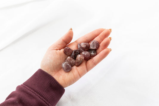 Hand holding pink coloured tumblestones on a white background