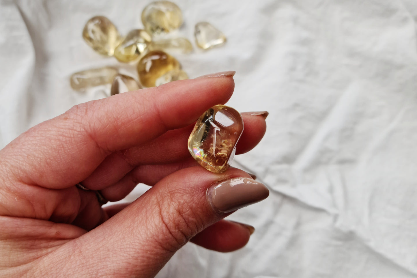 Hand holding a citrine crystal tumblestone against a white fabric background