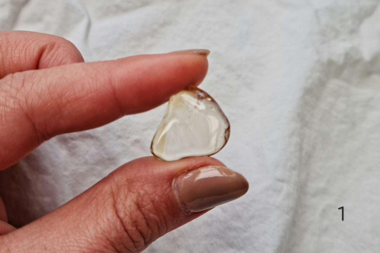 Hand holding a citrine crystal tumblestone against a white fabric background
