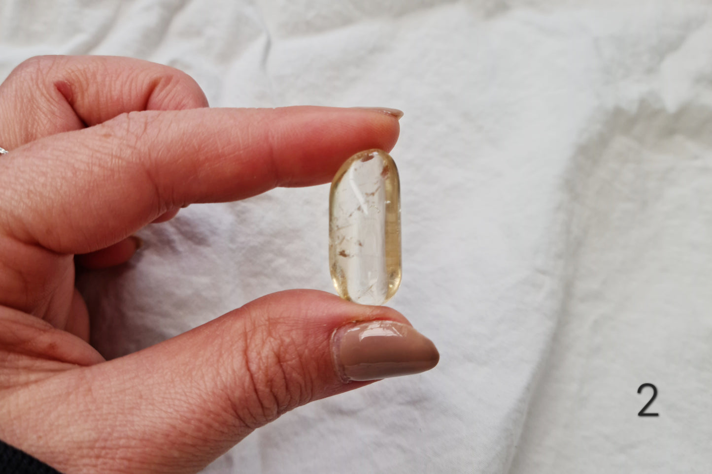 Hand holding a citrine crystal tumblestone against a white fabric background