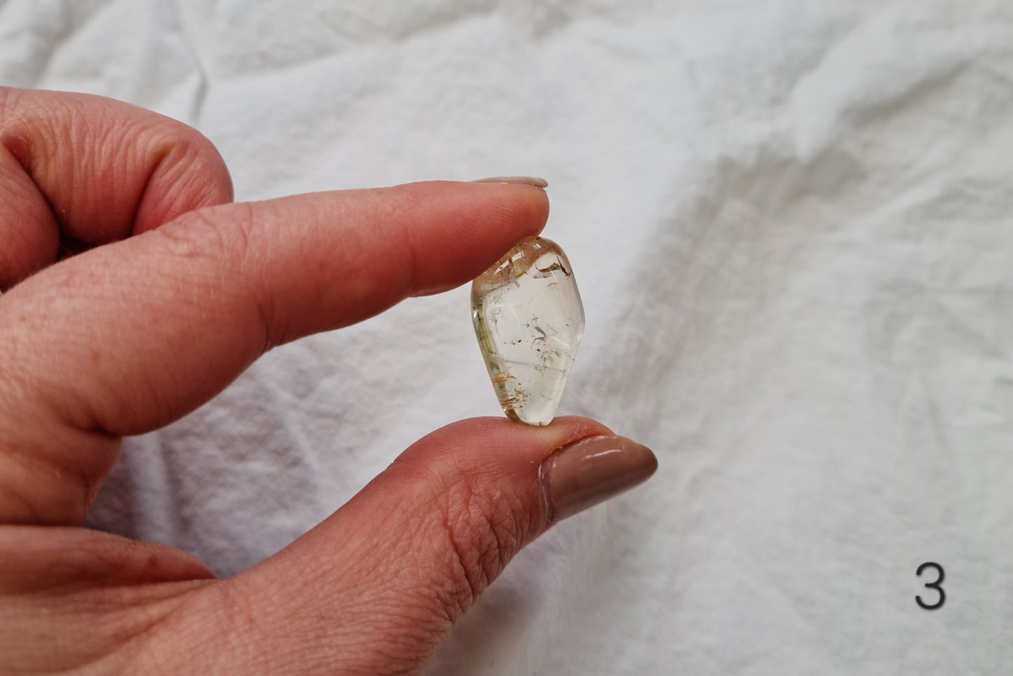 Hand holding a citrine crystal tumblestone against a white fabric background