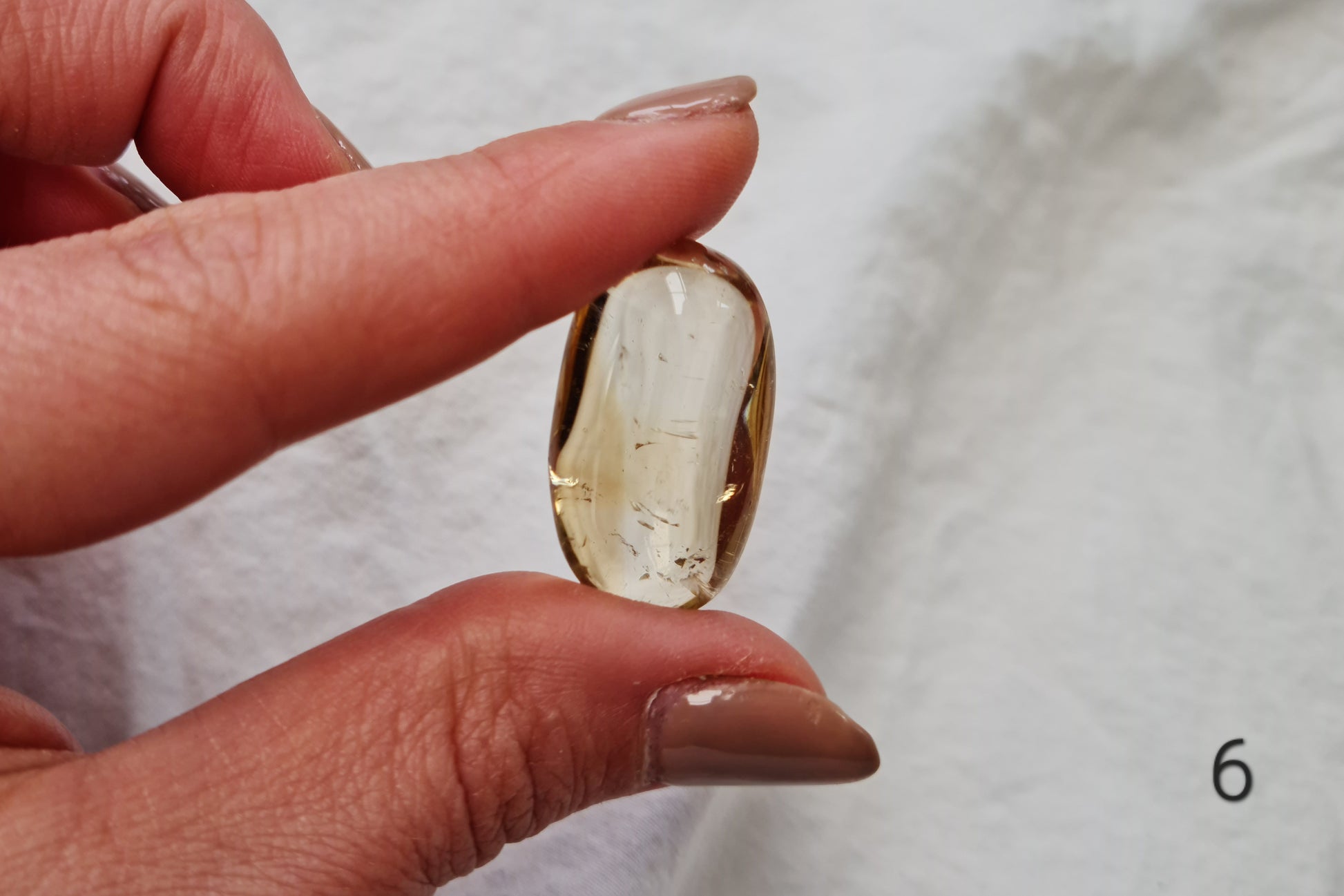 Hand holding a citrine crystal tumblestone against a white fabric background