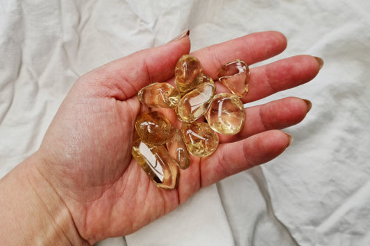 Hand holding natural citrine crystal tumblestones against a white fabric background