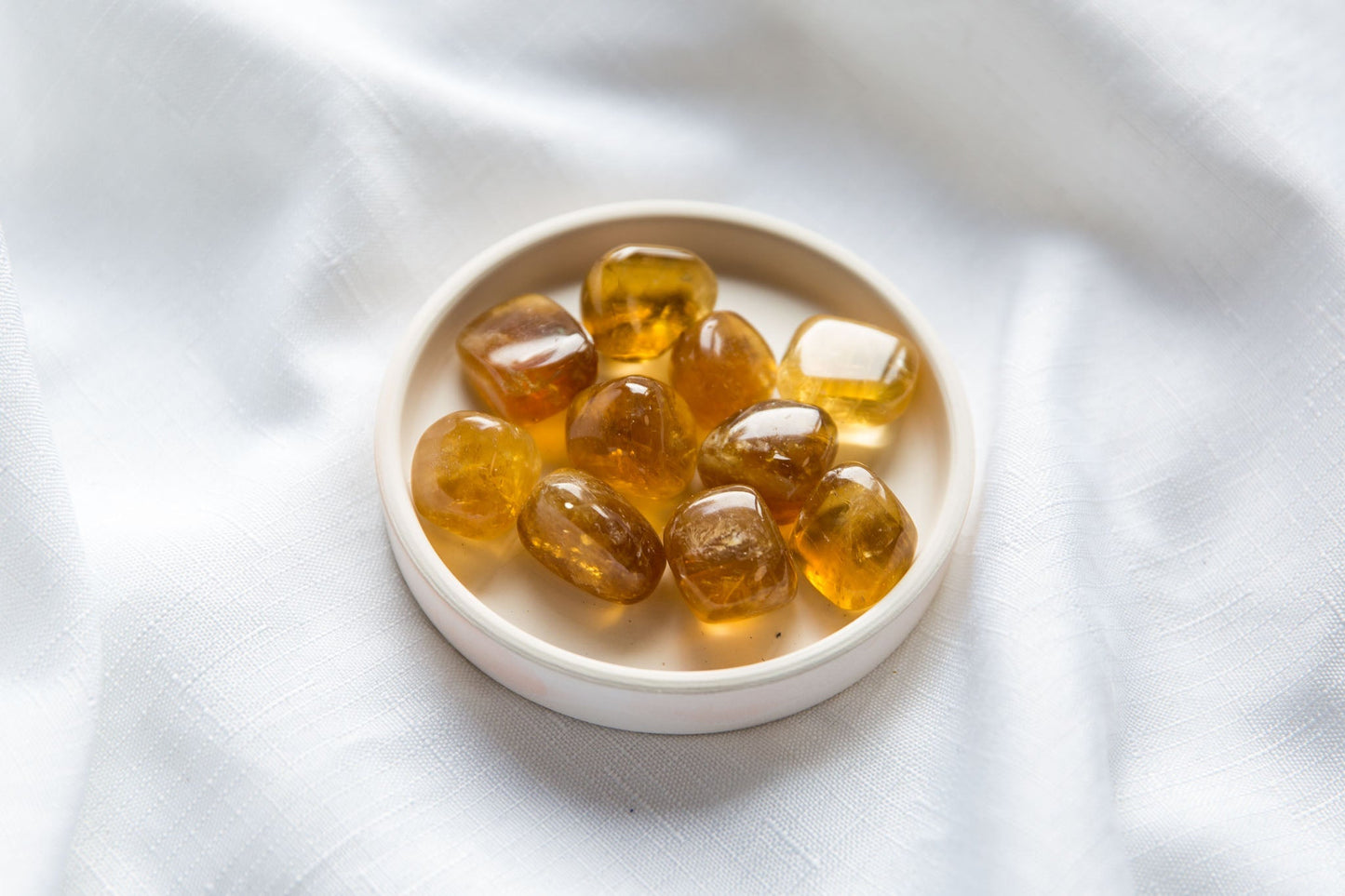 Honey Calcite Tumbles on a white dish sitting on a white cloth background