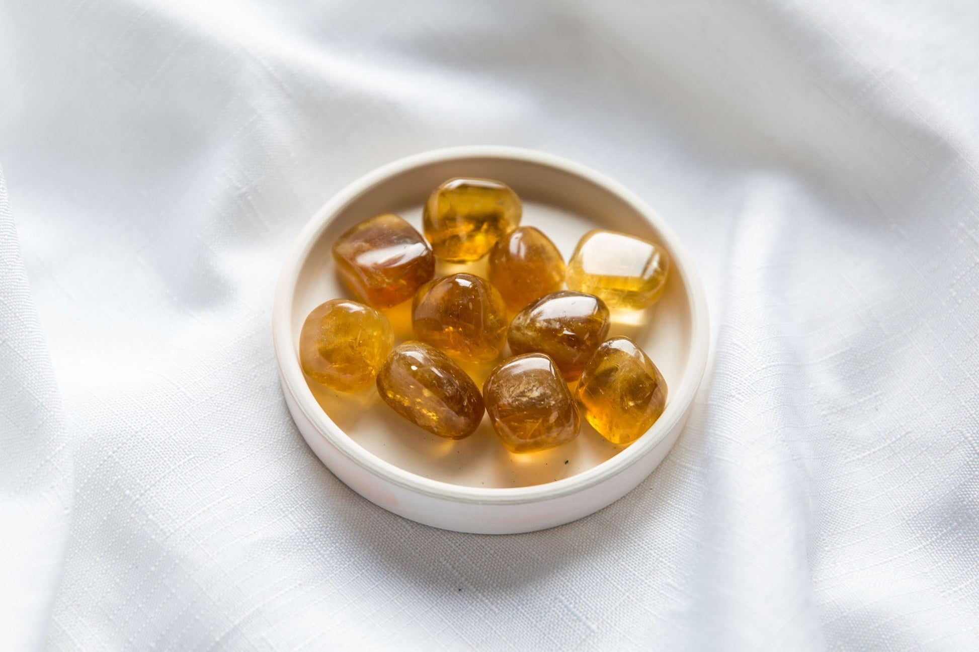 Honey Calcite Tumbles on a white dish sitting on a white cloth background